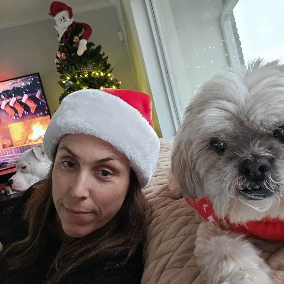 Momma in a Santa hat with Paris by the lit Christmas tree, Misty on the screen behind them.