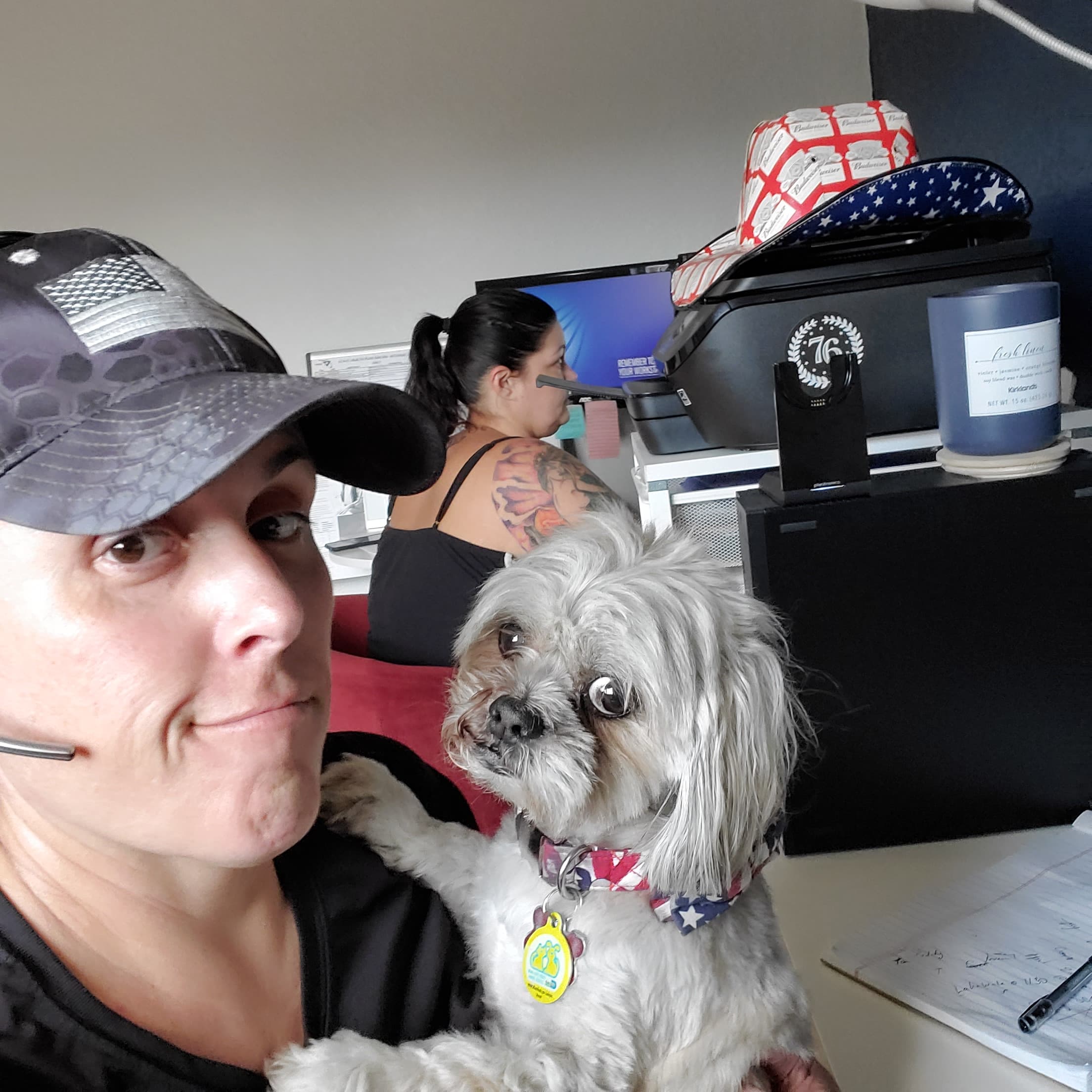 Momma at her home office desk in a headset with Paris on her lap, dual monitors behind them
